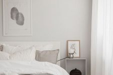 a beautiful minimalist bedroom with a monochromatic color scheme, light grey walls, a creamy bed with grey and white bedding, a wall-mounted nightstand and a floor lamp