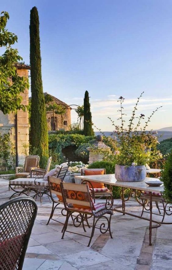 a bold Provence terrace with vintage forged furniture, a table with a stone tabletop, greenery and blooms and striped textiles a bold Provence terrace with vintage forged furniture, a table with a stone tabletop, greenery and blooms and striped textiles