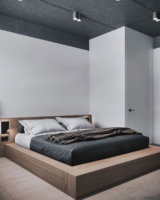 a chic minimal bedroom with a platform plywood bed with built in lights, lights on the ceiling and monochromatic bedding