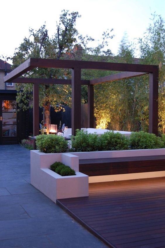 a chic minimalist terrace with a wooden deck, built-in benches and potted greenery, some lanterns is a lovely space to spend some time