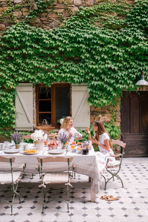 a fab Provence terrace clad with tiles, with a large table and neutral chairs, printed textiles and vines covering the wall of the house a fab Provence terrace clad with tiles, with a large table and neutral chairs, printed textiles and vines covering the wall of the house