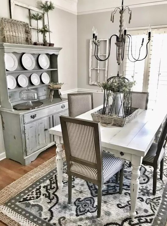 a greyish dining room inspired by Provence with a whitewashed buffet, a white table, striped chairs and a vintage chandelier