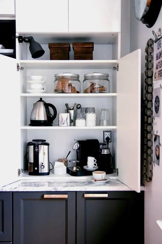a home tea and coffee bar with all the necessary appliances and various cups and cookies hidden inside a kitchen cabinet