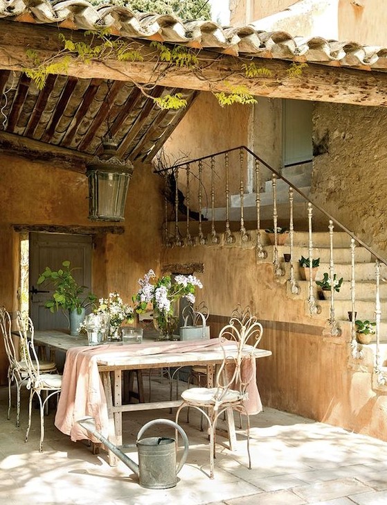 a large farmhouse table and white forged chairs, a large lantern over them, a watering can and some greenery and blooms to highlight that refined French feel a large farmhouse table and white forged chairs, a large lantern over them, a watering can and some greenery and blooms to highlight that refined French feel