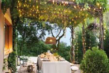 a lovely Provence terrace with wooden benches and a table, baskets with pillows, a woven pendant lamp and some lights over the space