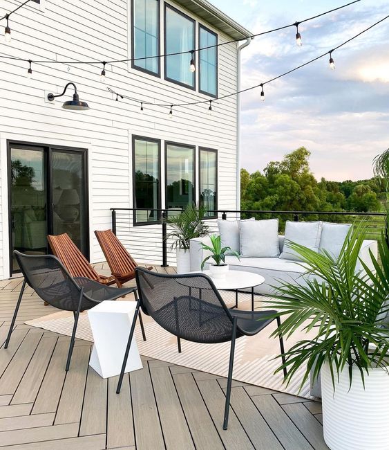 a lovely minimalist terrace with chevron wooden floors, a white low sofa, metal and wooden chairs, a sculptural side table and potted plants