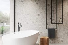 a minimalist bathroom with a glass wall, a bathtub on a stone platform, a stone wall and cool towel hangers