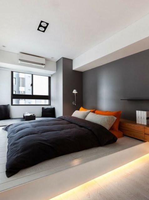 a minimalist bedroom with a grey accent wall, a platform bed with built in lights, lamps and black and bright textiles
