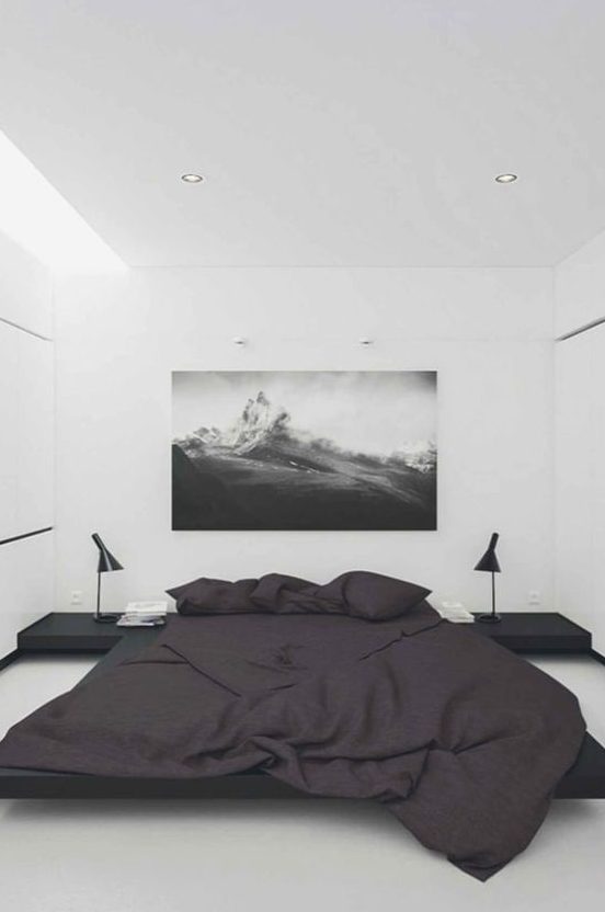 a minimalist bedroom with white walls, a black bed and nightstands plus lamps and a statement artwork