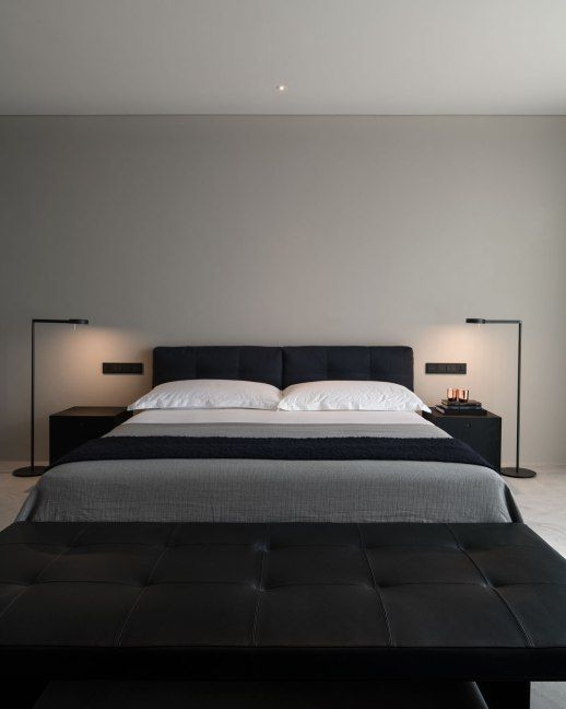 a minimalist contrasting bedroom with a black upholstered bed, a black leather bench, black nightstands and lamps