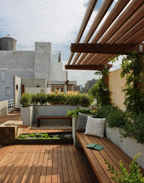 a minimalist deck with built-in benches, potted greenery and pillows and a little pond with a fountain is a cool space to be