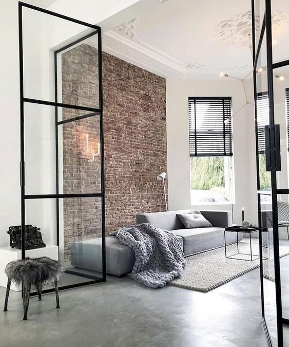 a minimalist living room with a brick wall, a grey sofa, a black coffee table and black shades