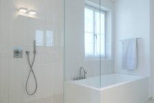 a minimalist neutral bathroom with largre scale and skinny tiles, a glass enclosed shower and a soak tub