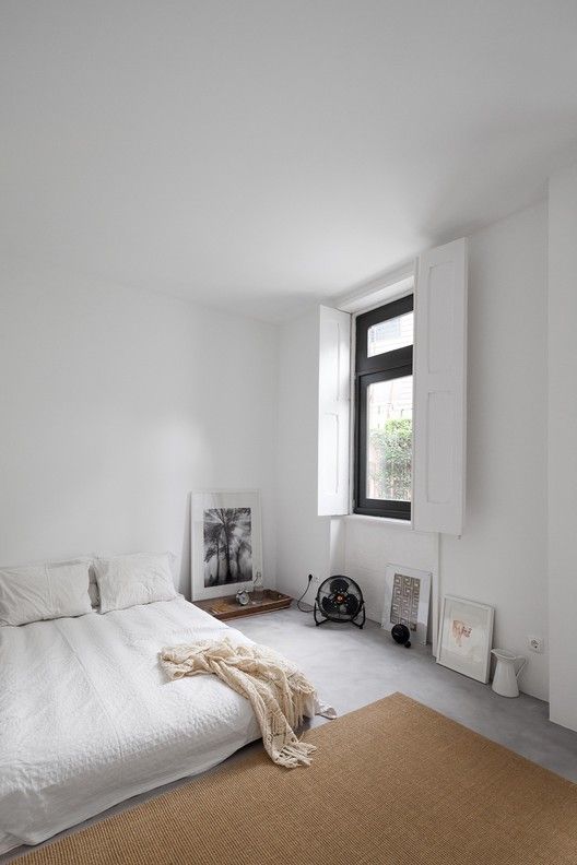 a minimalist neutral bedroom with a low bed with white bedding, a tan jute rug, some art and other stuff right on the wall