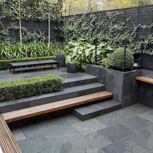 a minimalist terrace clad with stone tiles, a built-in bench, a black bench, planters and lots of greenery to make the space look fresh