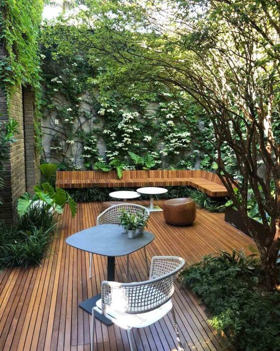 a minimalist terrace fully clad with stained wood, with metal tables and chairs, with a wooden stool and living walls and greenery growing here