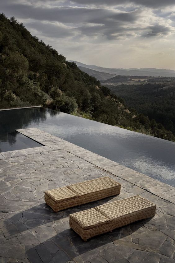 a minimalist terrace with a stone deck and woven daybeds plus a long pool and a forest view is a gorgeous space and you need nothing more