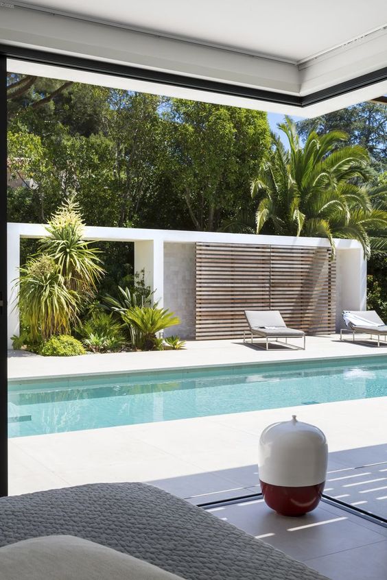 a minimalist terrace with grey loungers, growing greenery and trees and a plank wooden screen are all you need for a cool space