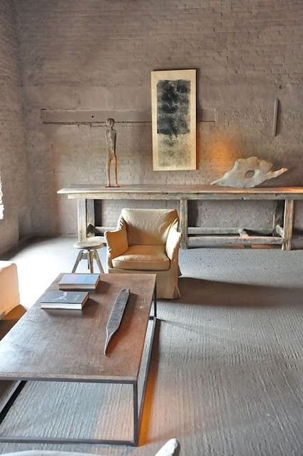 a minimalist wabi sabi living room in neutrals with brick walls, a concrete floor and rough and brutal furniture