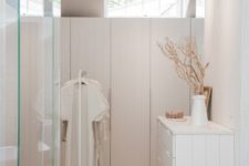 a minimalist white closet done with sleek wardrobes, a dresser that matches and a makeshift part plus glass doors