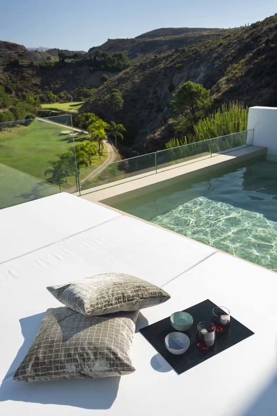 a mnimalist deck by the pool, with white cushions, some pillows and a tray with drinks - who needs more for a good rest