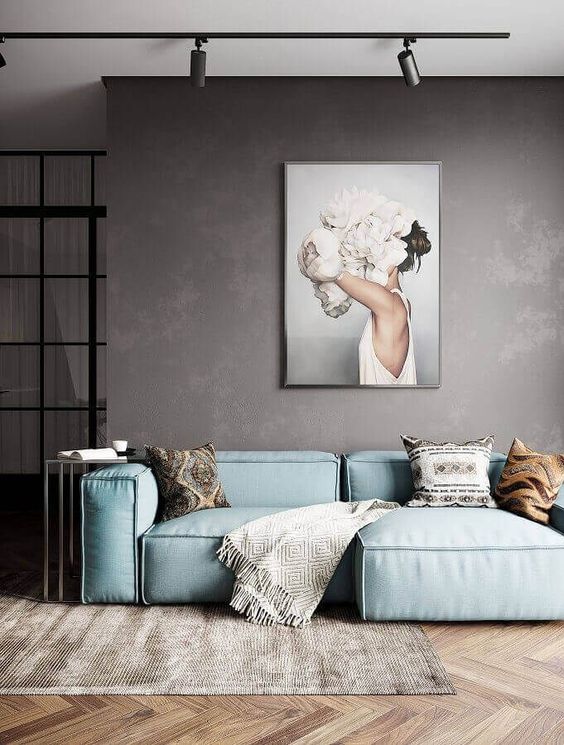 a moody minimalist living room with an aqua sofa, an artwork, a rug and chevron clad wooden walls