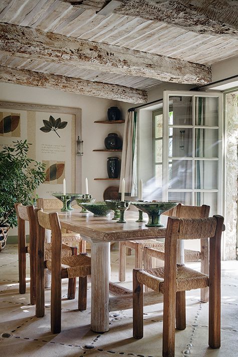 a neutral and rustic Provence dining space with a whitewashed ceiling and beams, a stained table and chairs, corner shelves and greenery