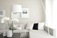 a neutral minimalist living room with an off-white sectional sofa, a floor lamp, artworks and potted blooms