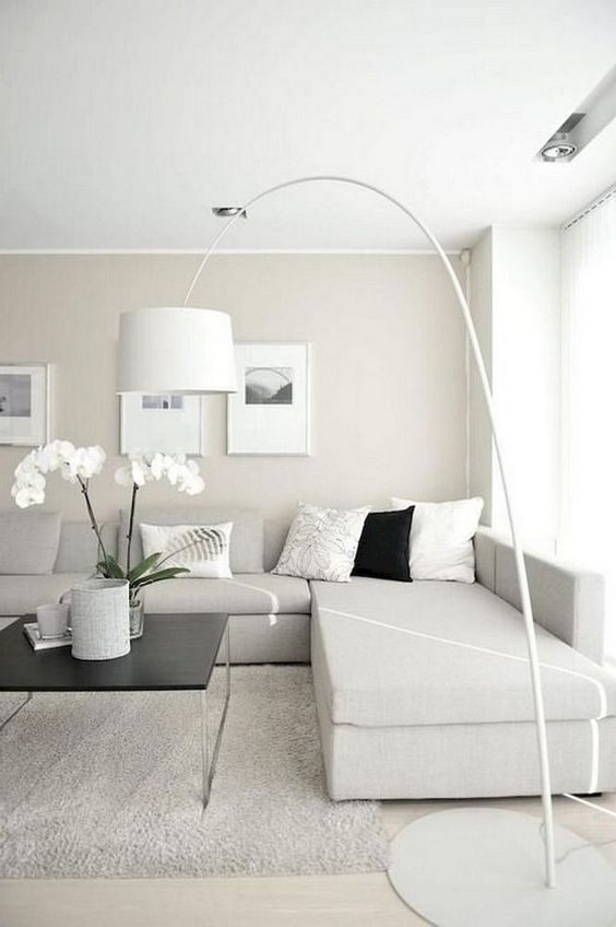 a neutral minimalist living room with an off-white sectional sofa, a floor lamp, artworks and potted blooms