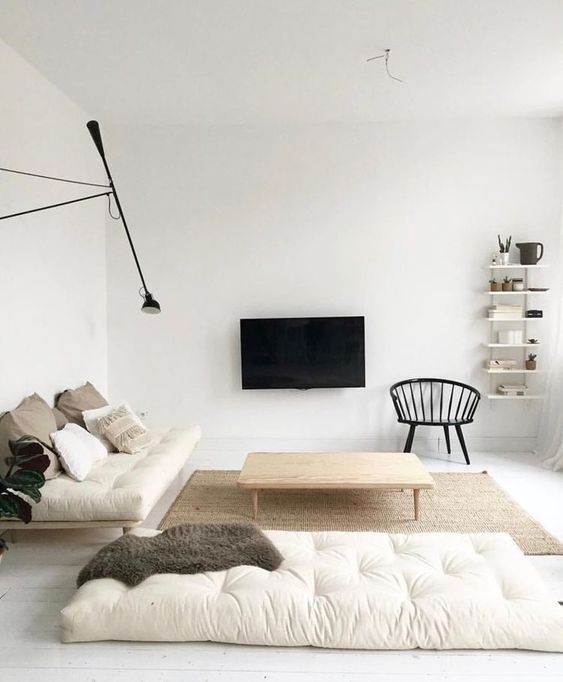 a neutral minimalist living room with off-white cushions, wooden furniture, a TV on the wall and a wall lamp