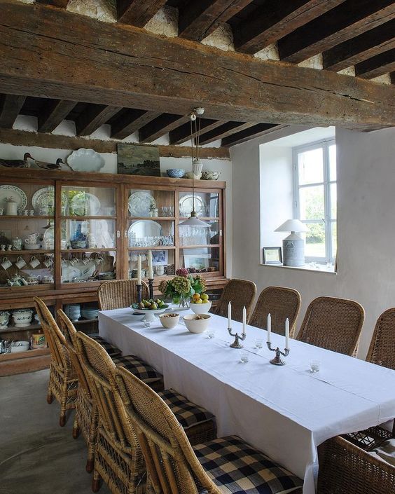 a rustic Provence dining room with a stained glass buffet, a long dining table and wicker chairs, wooden beams on the ceiling