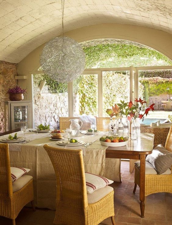 a rustic Provence dining room with an arched ceiling, a stained table and wicker chairs, a catchy chandelier and a corner cabinet