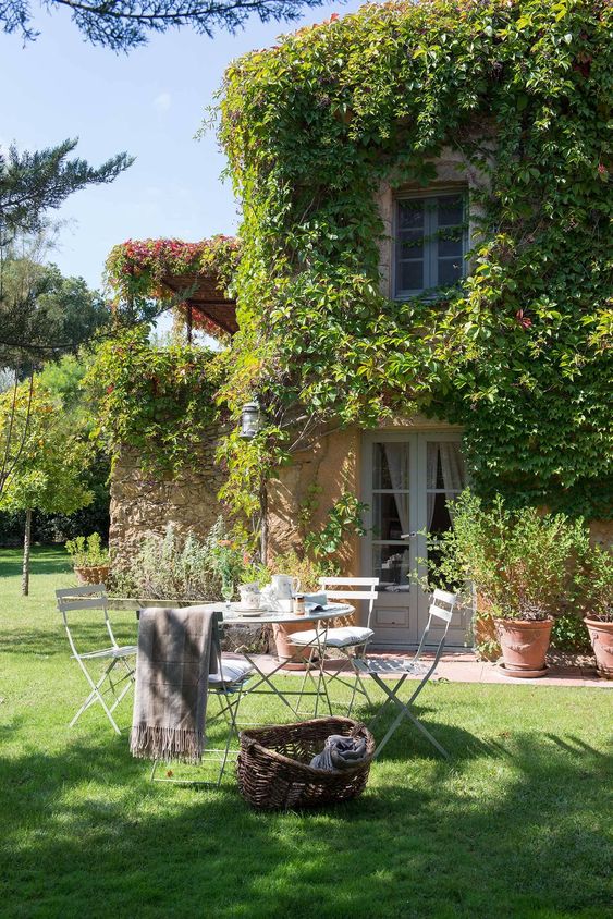 a simple Provence outdoor space with green lawn, a metal table and chairs, a basket for storage, a blanket and lots of greenery around