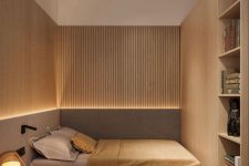 a small and minimal bedroom with wooden slab walls and built-in storage units, an upholstered bed and a long nightstand plus built-in lights