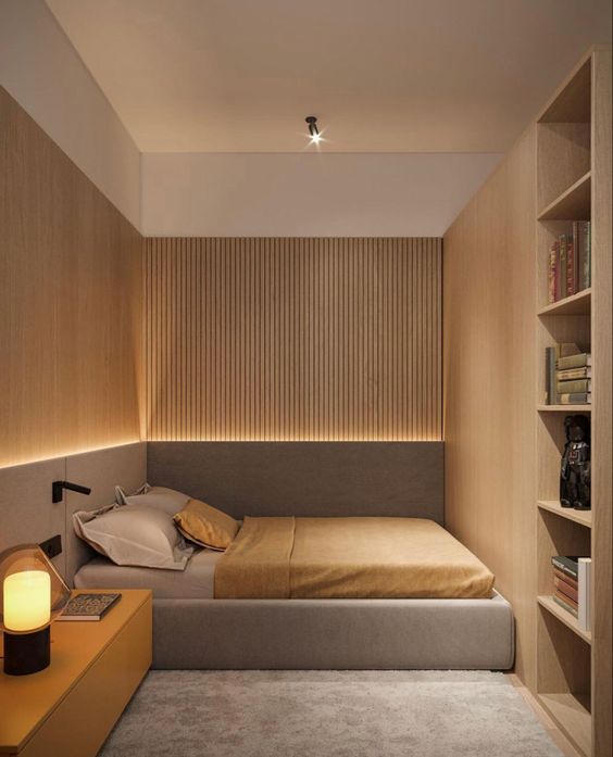 a small and minimal bedroom with wooden slab walls and built-in storage units, an upholstered bed and a long nightstand plus built-in lights