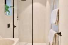 a small white minimalist bathroom clad with tiny tiles, with a ladder for towels, white appliances and a shower with a glass partition