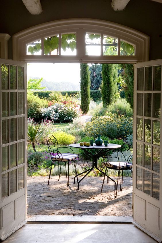 a small yet chic Provence outdoor space with a metal roudn table and forged chairs with striped cushions and lots of greenery and blooms around