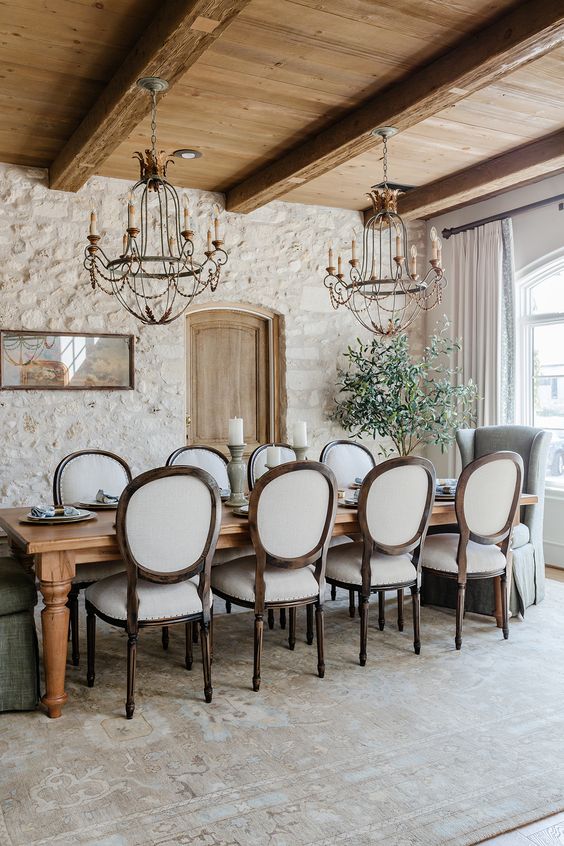 a sophisticated Provence dining space with stone walls and a wooden ceiling and beams a stained table and vintage chairs vintage chandeliers