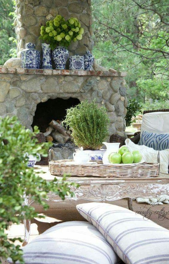 a stone fireplace with blue porcelain vases, a refined antique table and striped pillows, potted greenery and green hydrangeas