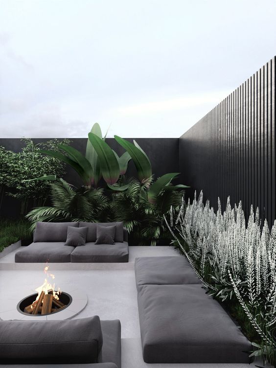 a stylish and ultra-minimalist terrace in neutrals, with black cushions and pillows, a fire pit, greenery and large plants is a very chic space