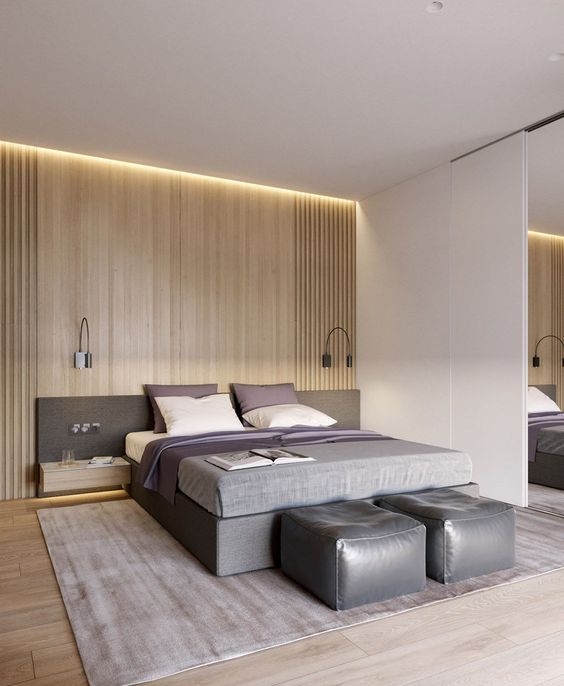 a stylish minimalist bedroom with a light-stained wall, a grey bed and floating nightstands, leather poufs and black wall sconces