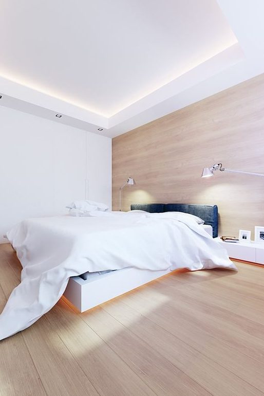 a stylish minimalist bedroom with a white raised bed with lights, an upholstered headboard, some lamps and a large sleek storage unit