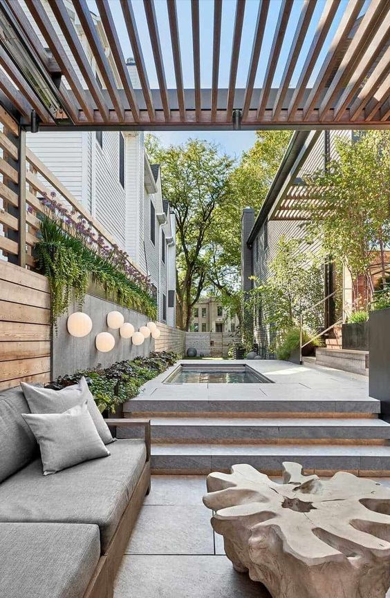 a super stylish minimalist terrace clad with stone tiles, with a pool, a wooden sofa with grey upholstery and a coffee table of piece of wood