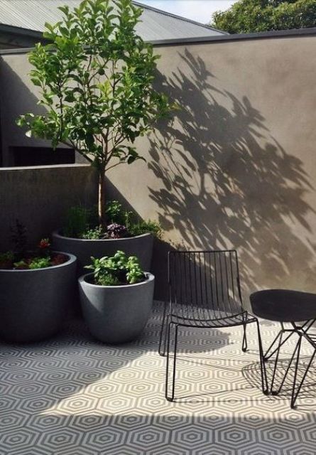 a tiny minimalist terrace with geo tiles, concrete planters with greenery and trees, a black table and a black chair