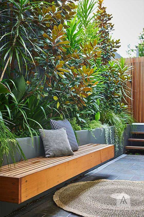 a very simple and minimalist terrace clad with concrete tiles, with concrete tall planters for greenery and bushes, a floating bench and a small ladder