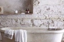 a wabi-sabi bathroom in neutrals with stone wall, a stone tub and a jute rug looks very roough and imperfect