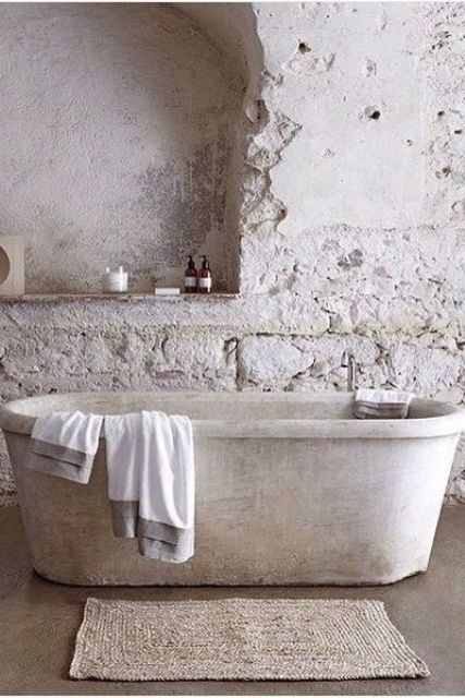 a wabi-sabi bathroom in neutrals with stone wall, a stone tub and a jute rug looks very roough and imperfect