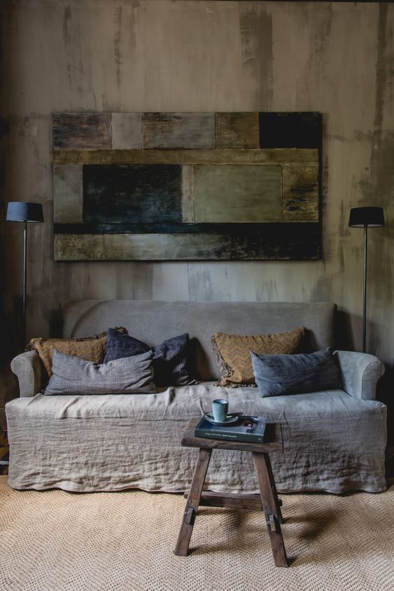a wabi sabi interior with a rough wooden wall, a wooden wall art of rough elements and a coarse textile sofa