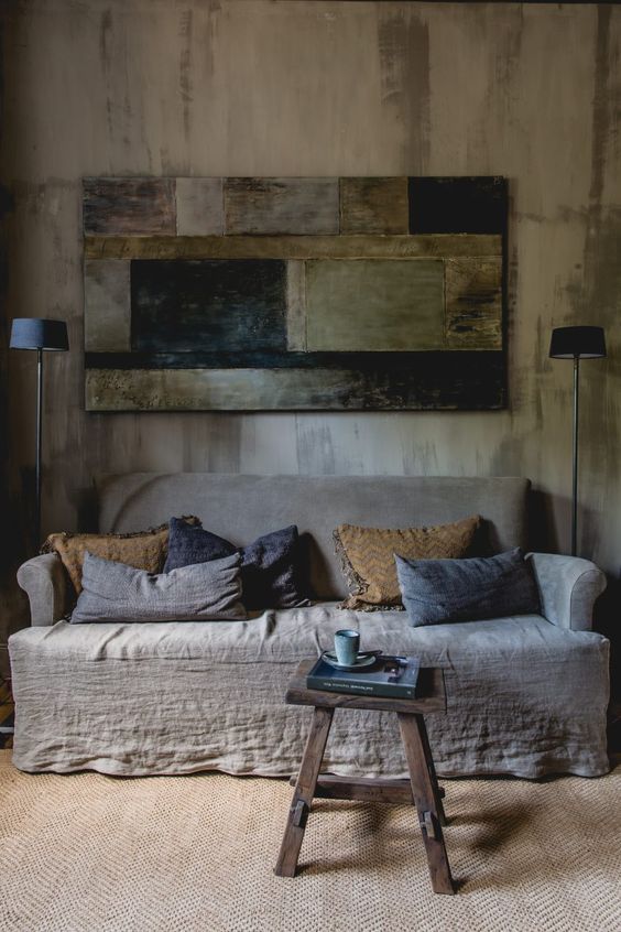 a wabi-sabi interior with a rough wooden wall, a wooden wall art of rough elements and a coarse textile sofa