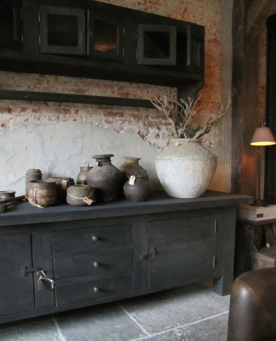 a wabi-sabi space with a rough brick wlal, a wooden cabinet, some rough stone vases and planters